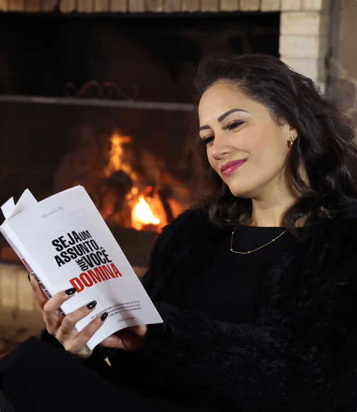 Autora Miranda Ely segurando seu livro Seja um assunto que você domina em frente a uma lareira